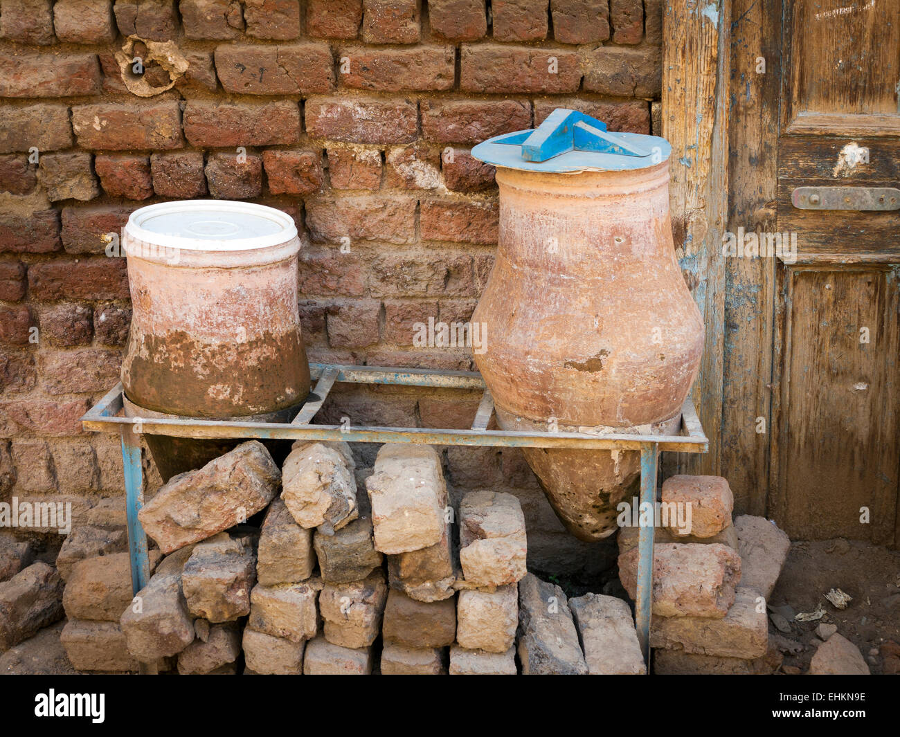 La poterie de l'eau potable publique 2 1 transporteurs avec couvercle bleu sur support métallique à l'extérieur d'un mur de brique de boue et de bois de l'Afrique Égypte Banque D'Images