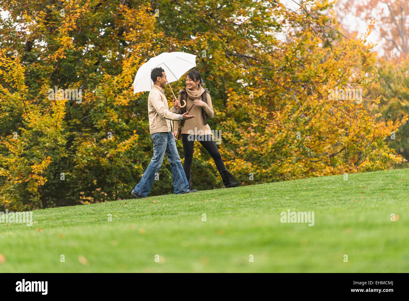 Couple walking with umbrella in park Banque D'Images