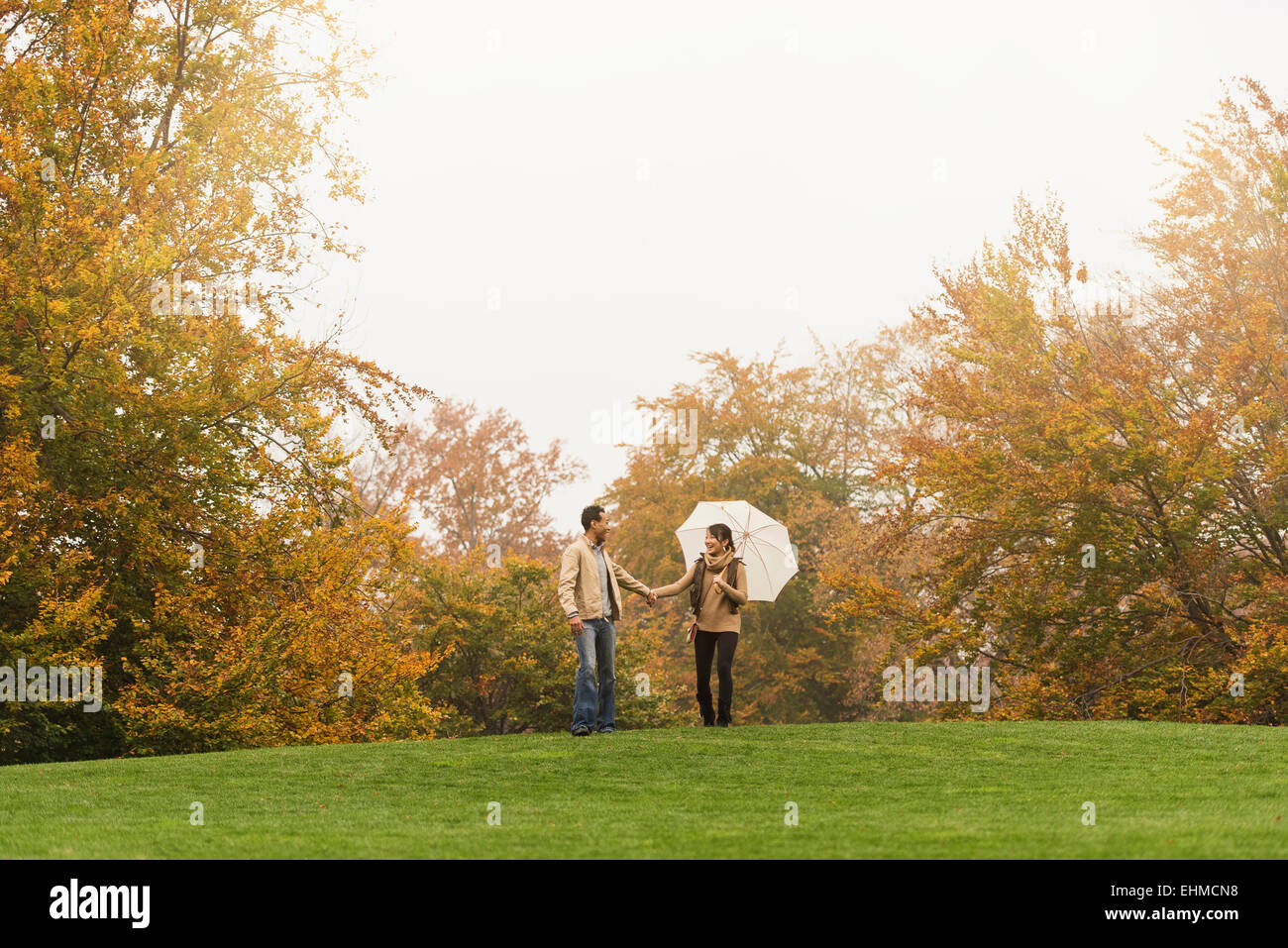 Couple walking with umbrella in park Banque D'Images