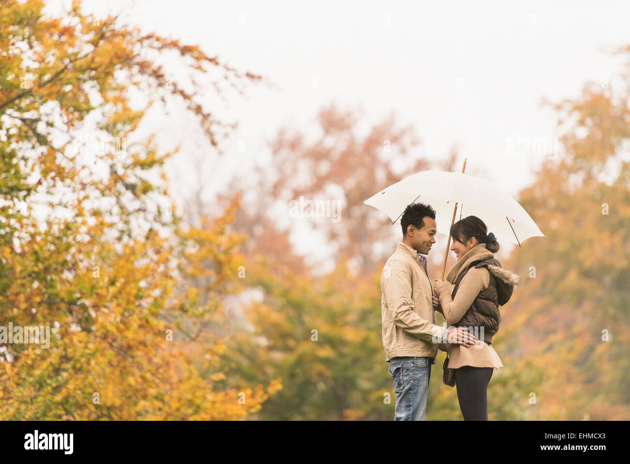 Couple standing with umbrella in park Banque D'Images
