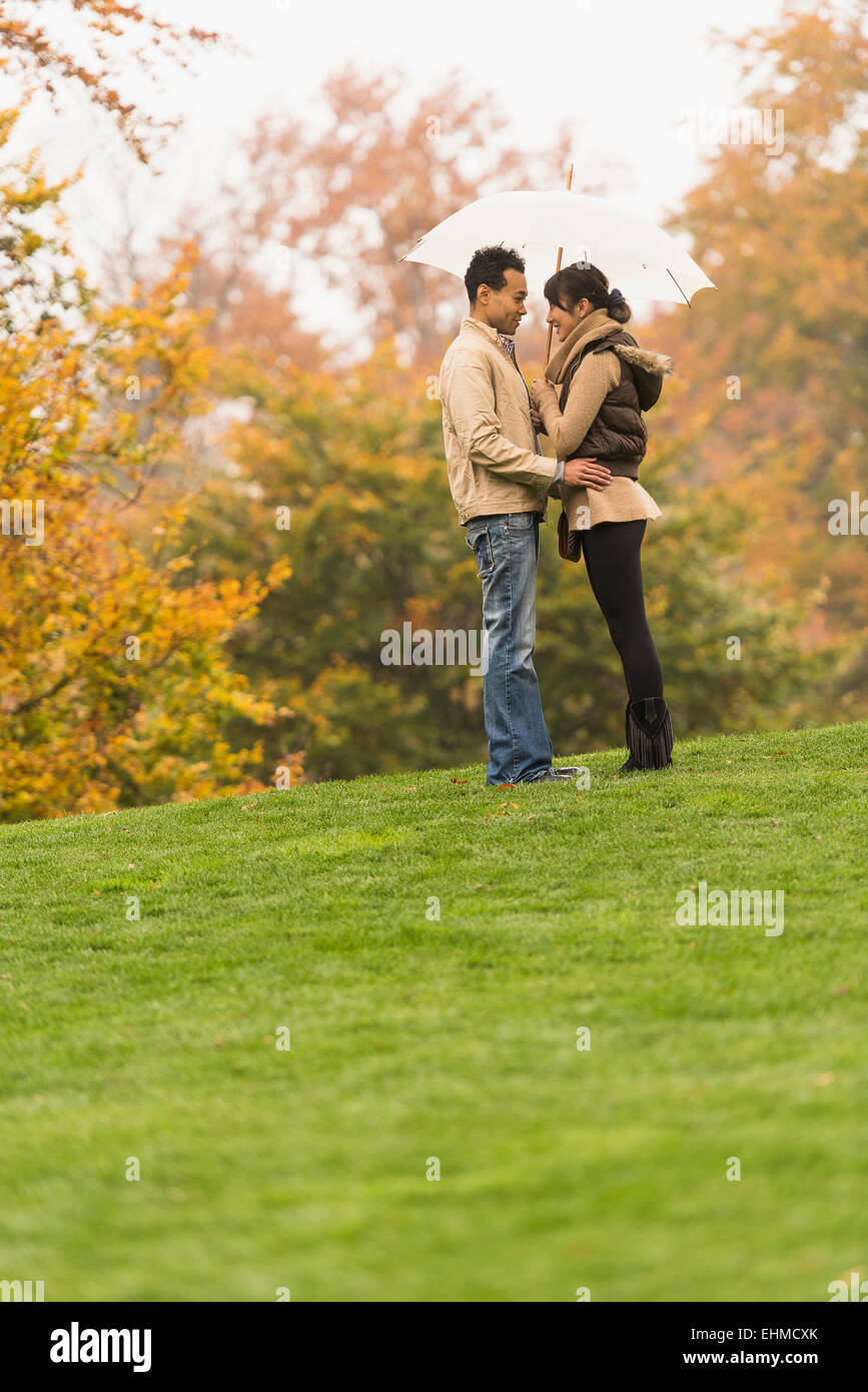 Couple standing with umbrella in park Banque D'Images