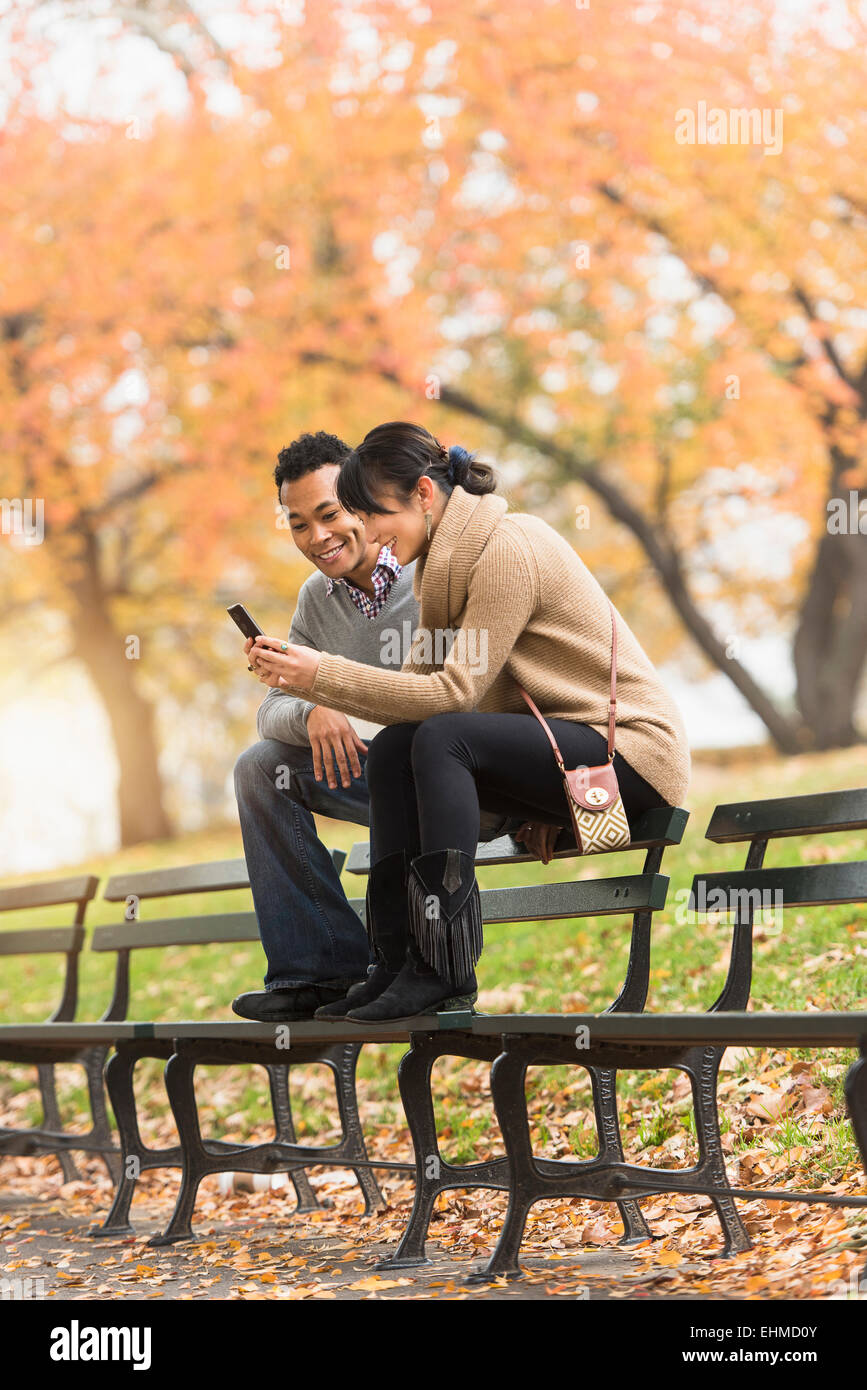 Couple using cell phone on park bench Banque D'Images