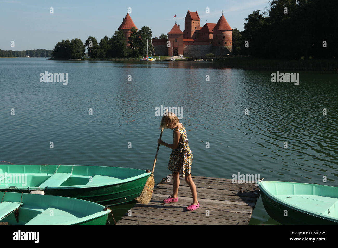 Jeune fille balaye l'embarcadère du lac Galve avec l'île de Trakai Castle dans le fond près de Vilnius, Lituanie. Banque D'Images