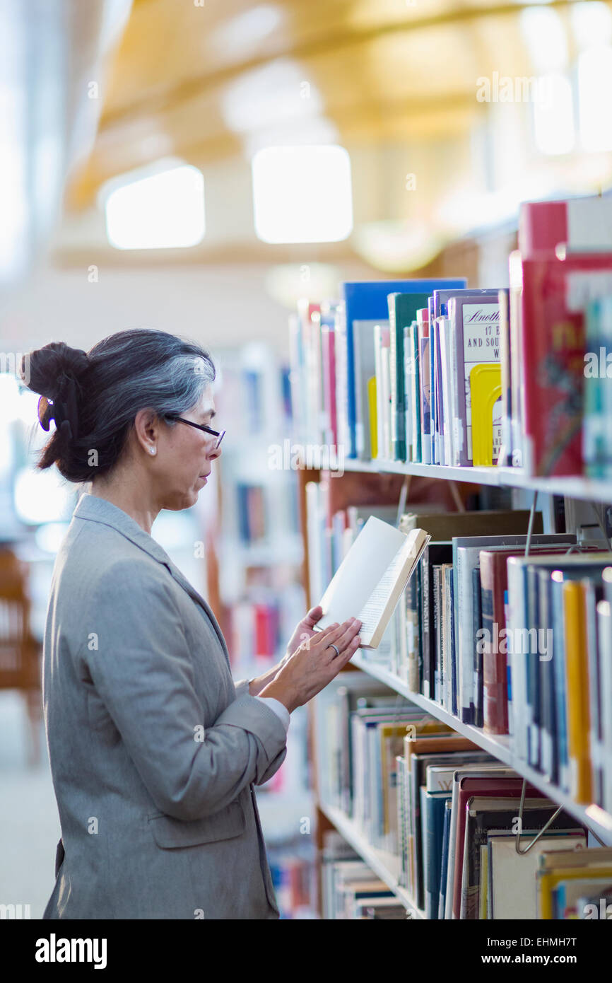 Older Hispanic woman reading book in library Banque D'Images