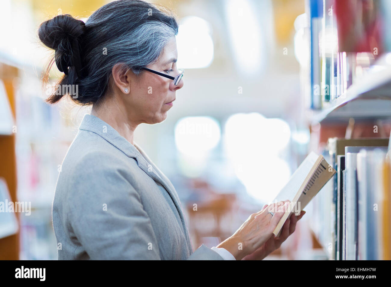 Older Hispanic woman reading book in library Banque D'Images