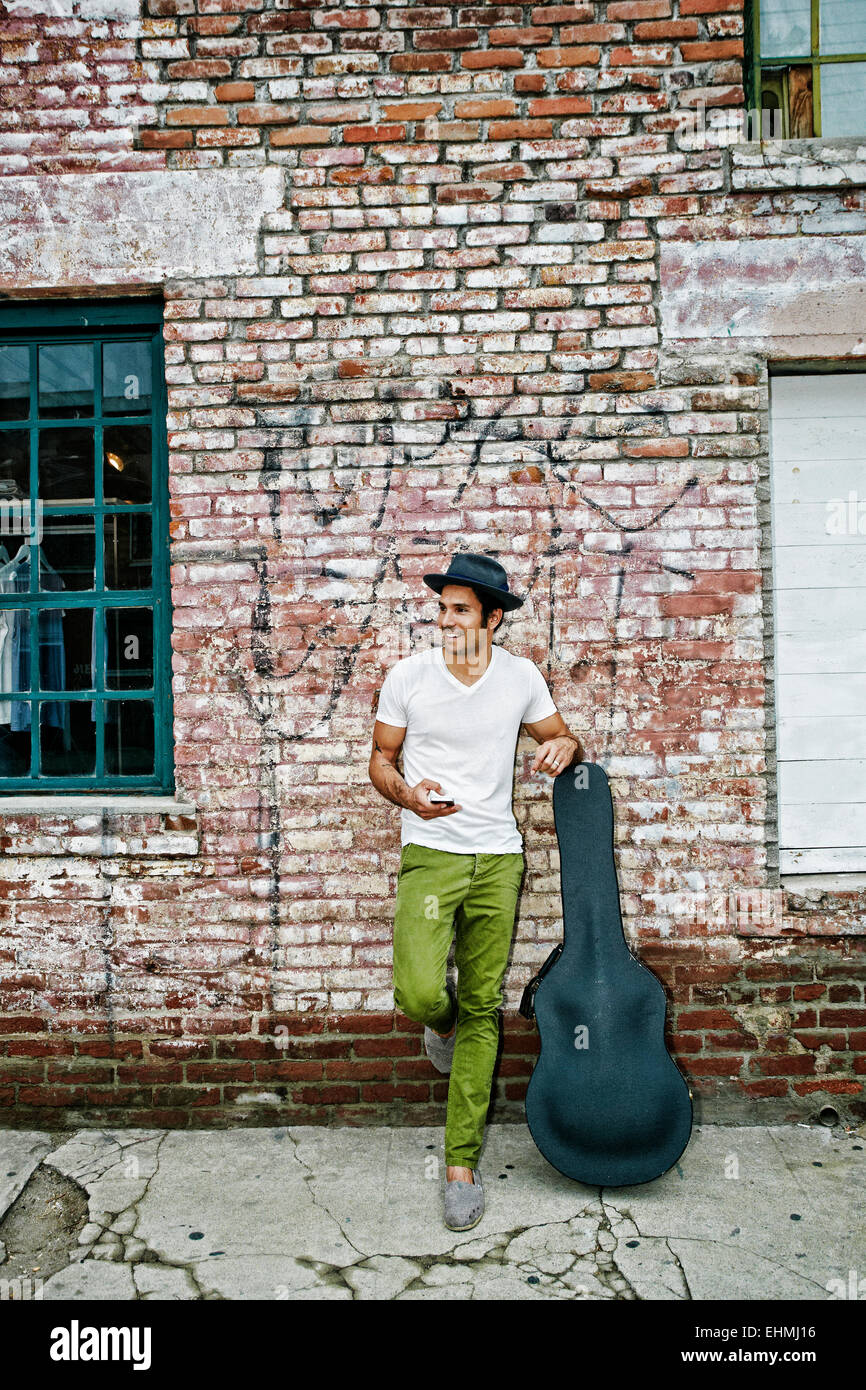 Mixed Race musicien avec étui à guitare using cell phone Banque D'Images