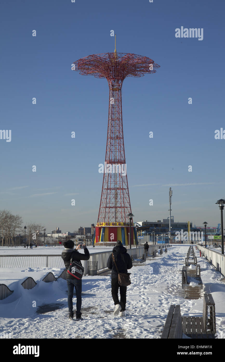 Les gens marchent sur la neige couverts pier avec le monument du saut en parachute de remplir le ciel à Coney Island, Brooklyn, New York. Banque D'Images