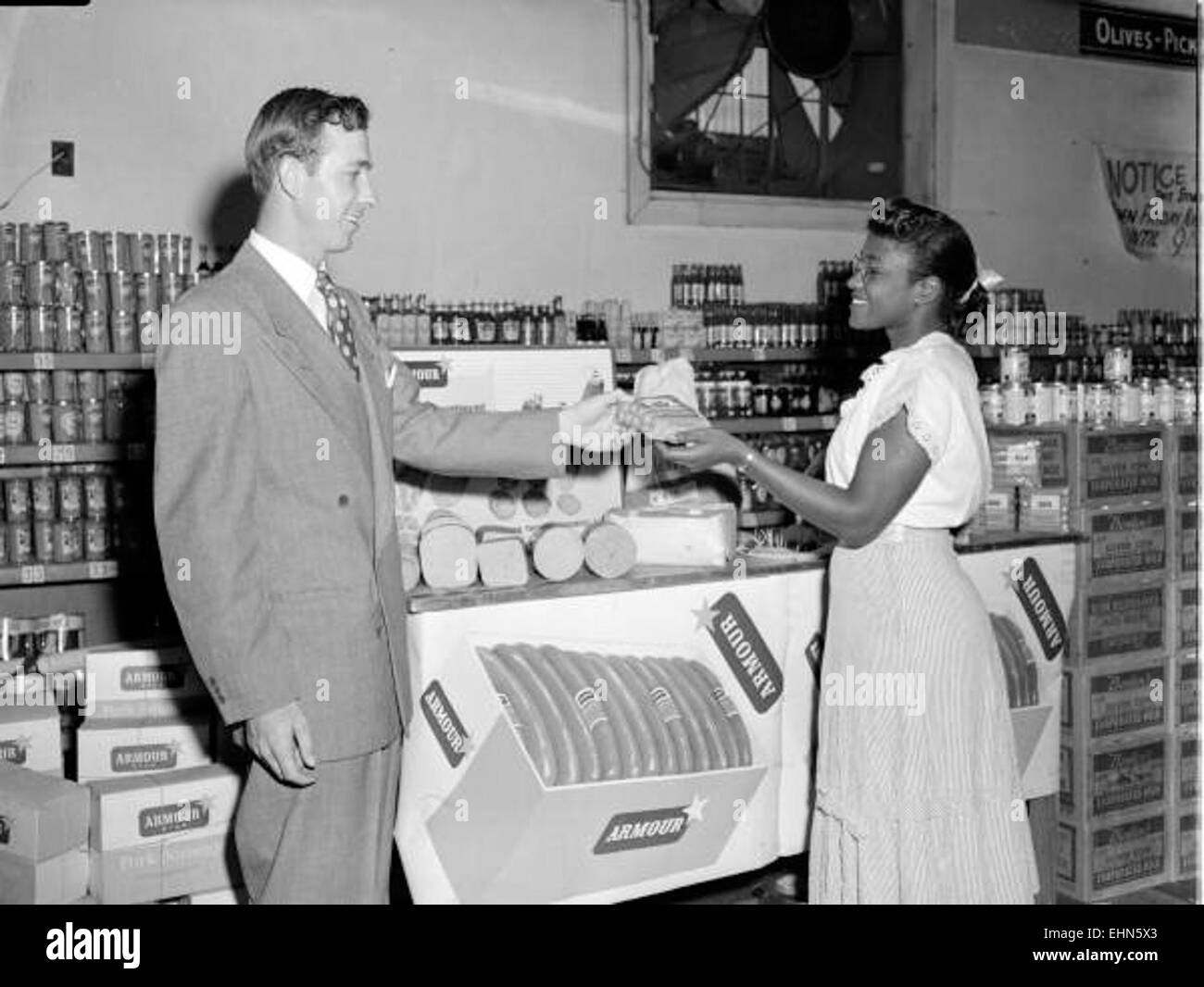 Sur cette image, Mr. Higgins remet des hot-dogs de marque Armour à un acheteur. Le moment capture un échange simple et quotidien dans un cadre d'épicerie, soulignant la popularité et la commodité des produits alimentaires prêts à cuire dans le commerce de détail moderne. Banque D'Images