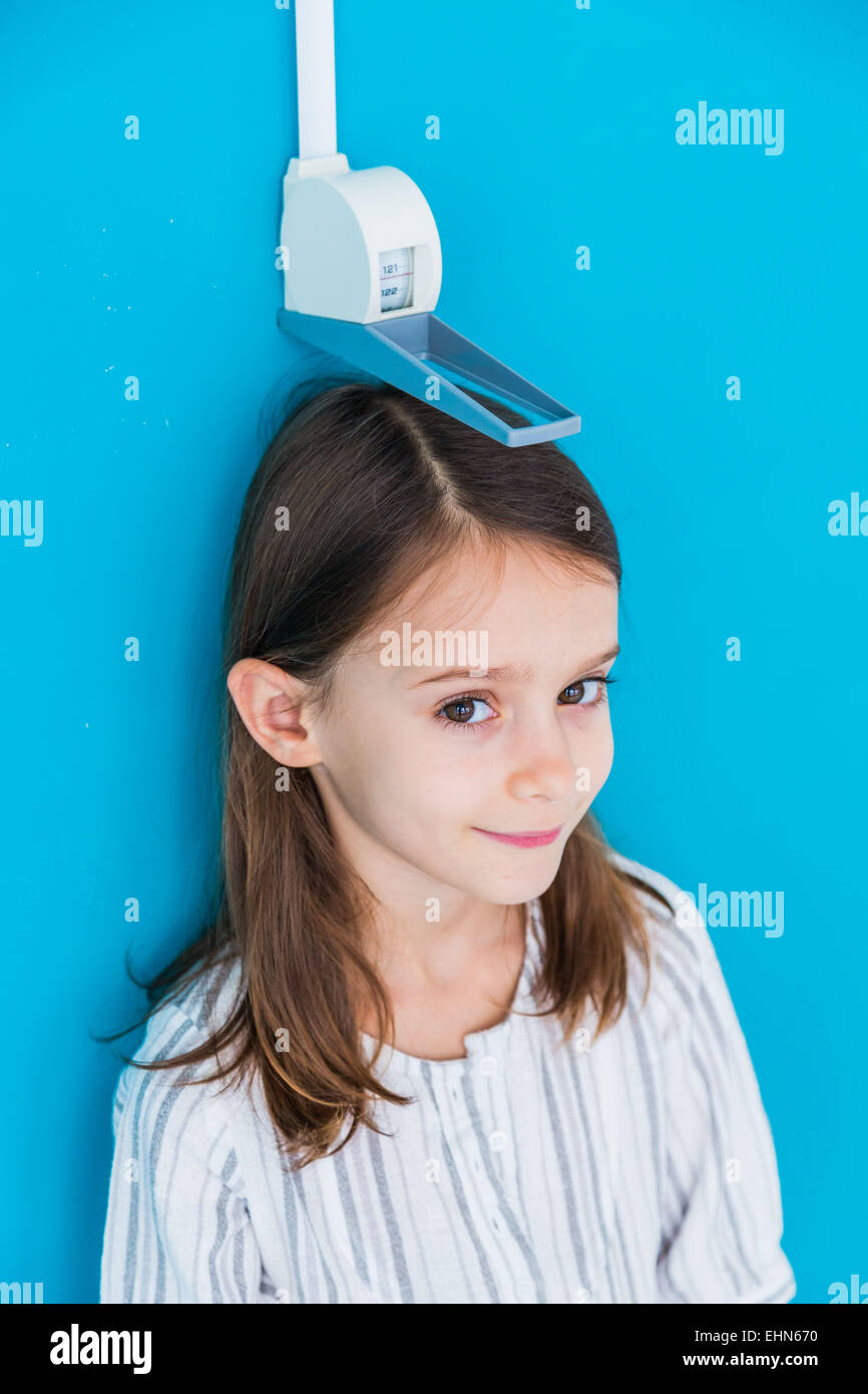 7-year-old girl measuring elle-même contre une jauge de hauteur. Banque D'Images