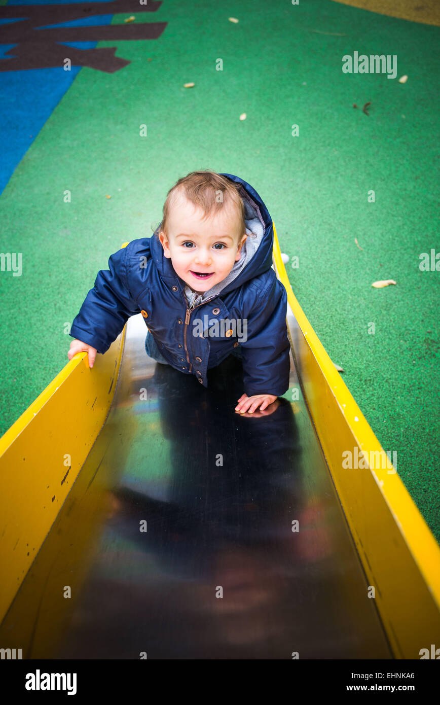 18 mois bébé garçon sur une diapositive dans une aire de jeux. Banque D'Images