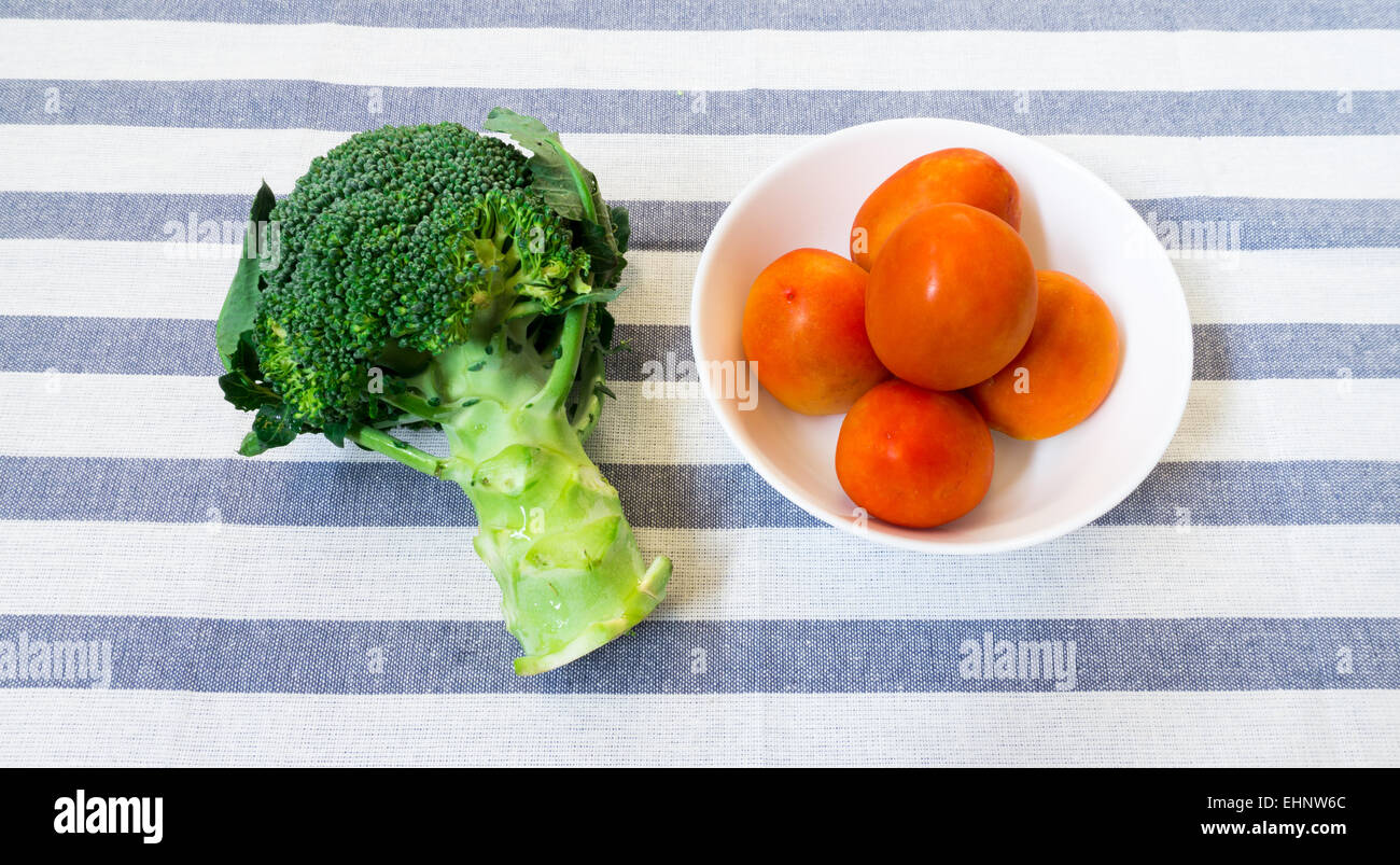 Cinq Tomates sur bol blanc sur fond à rayures avec brocoli Banque D'Images