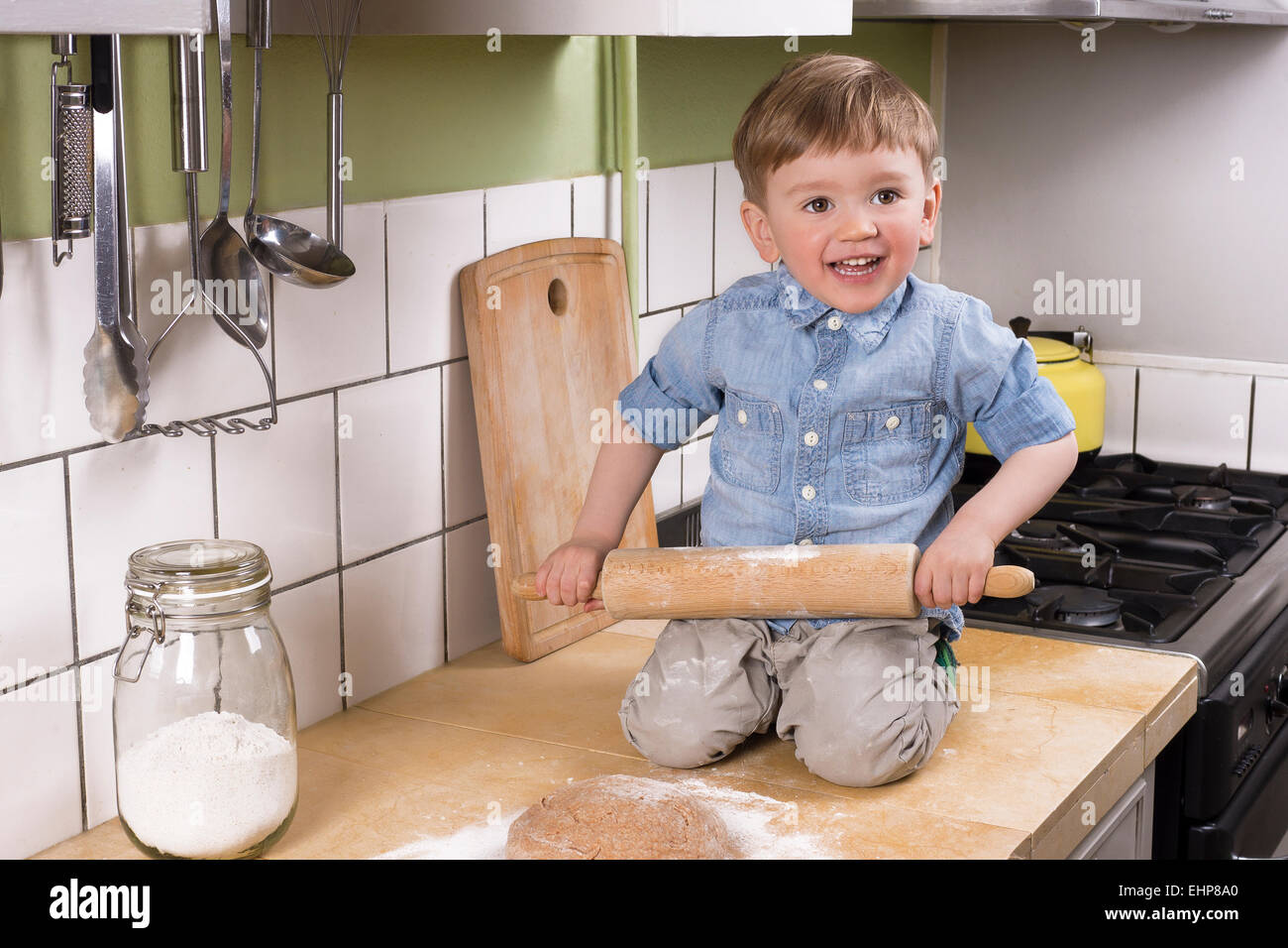 Petit garçon assis sur le comptoir de la cuisine avec la pâte à pizza et de rouleau à pâtisserie. Banque D'Images