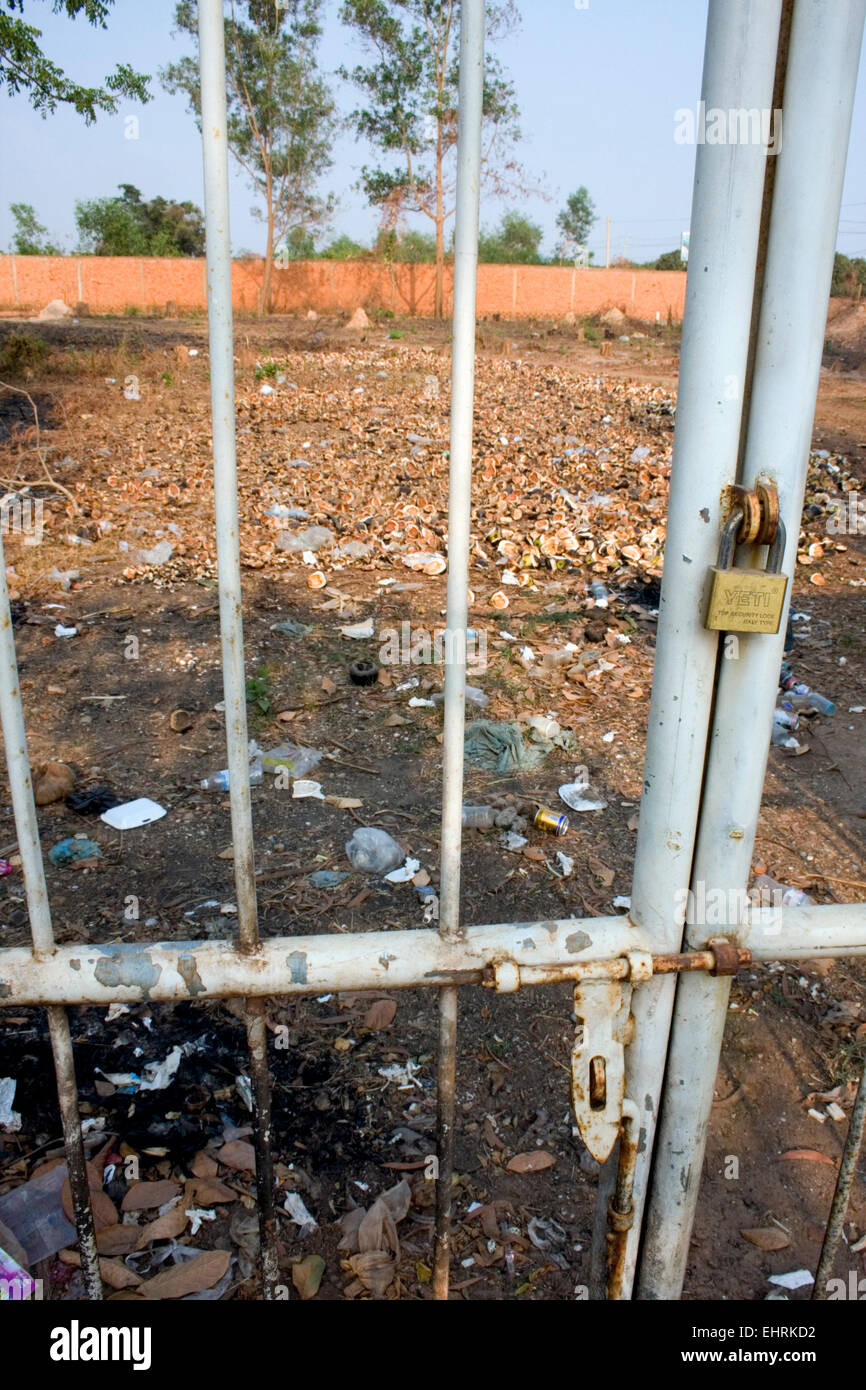 Un champ ouvert jonché d'ordures et les écorces de noix de coco est vu à travers une porte cadenassée à Skun, province de Kampong Cham, au Cambodge. Banque D'Images