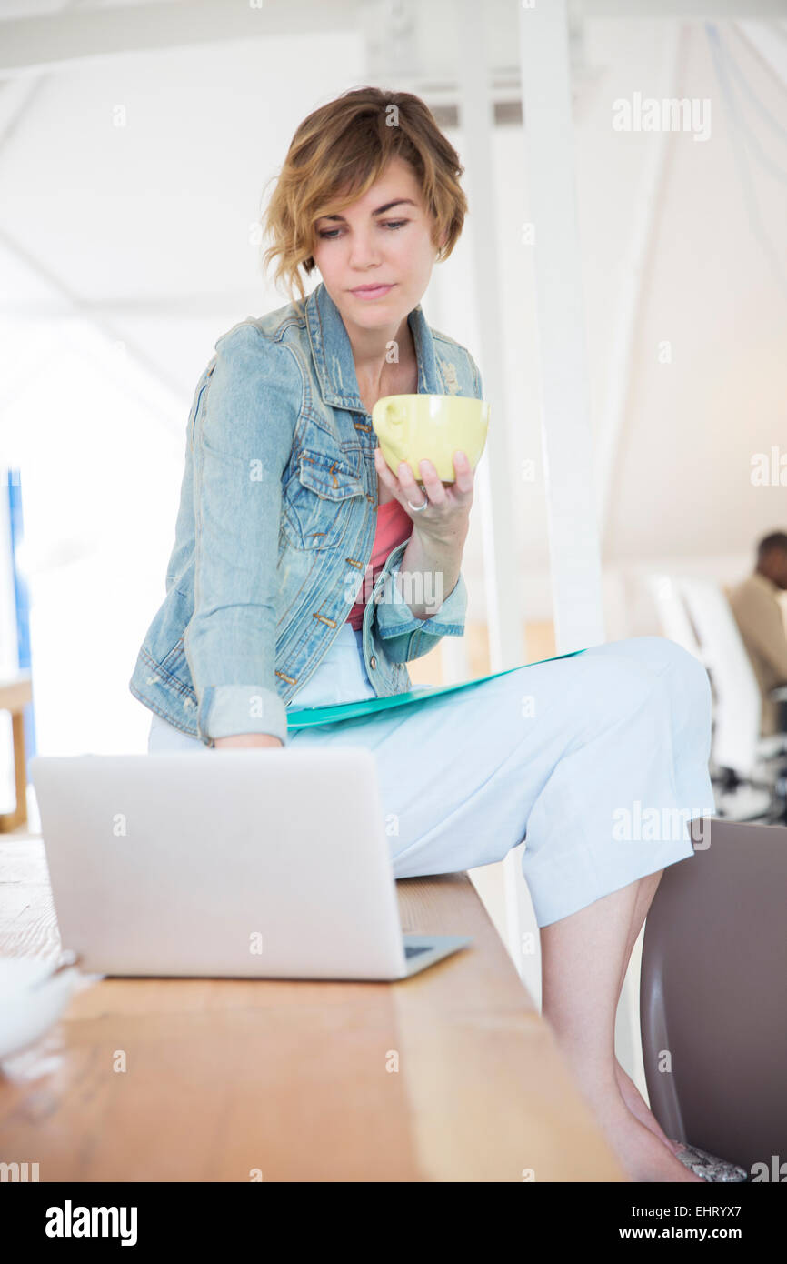 Employée de bureau avec du café à l'aide d'ordinateur portable Banque D'Images