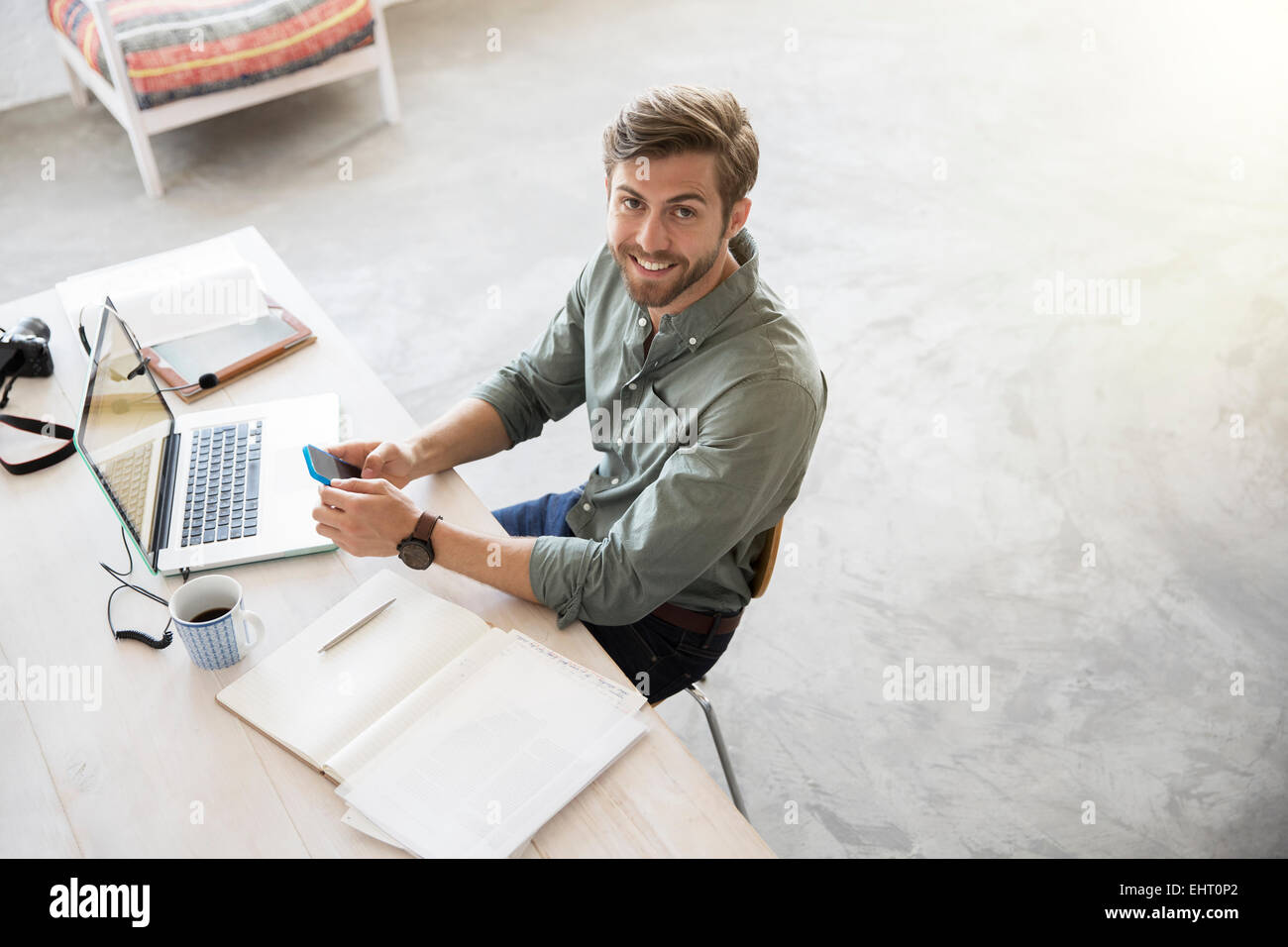 Portrait de jeune homme assis à un bureau avec téléphone mobile et ordinateur portable Banque D'Images