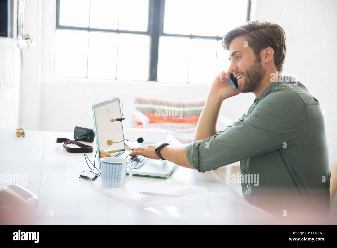 Portrait de jeune homme assis à un bureau avec téléphone mobile et ordinateur portable Banque D'Images