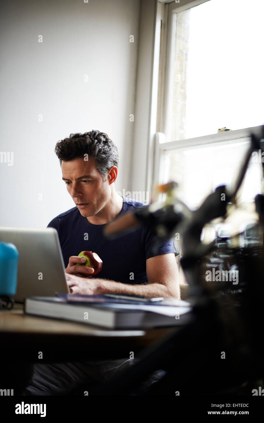 Man working on laptop at home eating apple Banque D'Images