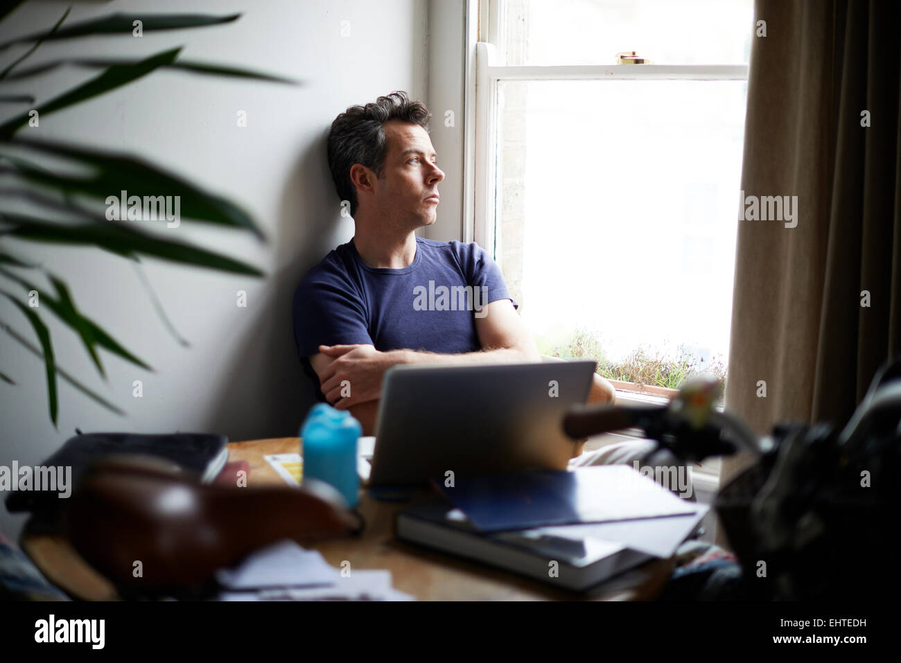 L'homme assis à table avec un ordinateur portable ouvert à la recherche d'une fenêtre Banque D'Images