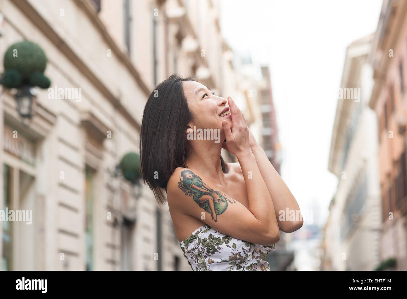 Belle jeune femme asiatique tatouage sur l'épaule avec sourire et parler à l'aide de téléphone mobile de plein air en milieu urbain Banque D'Images