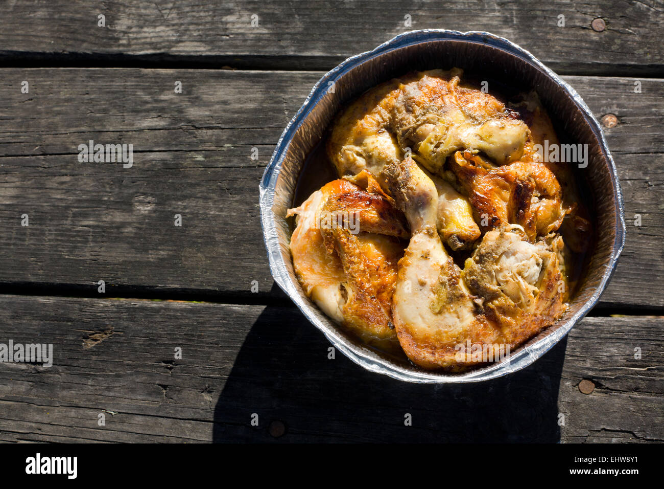 Poulet mariné grillé dans du papier aluminium bac. Couper en morceaux plus vieille table de pique-nique en bois Banque D'Images