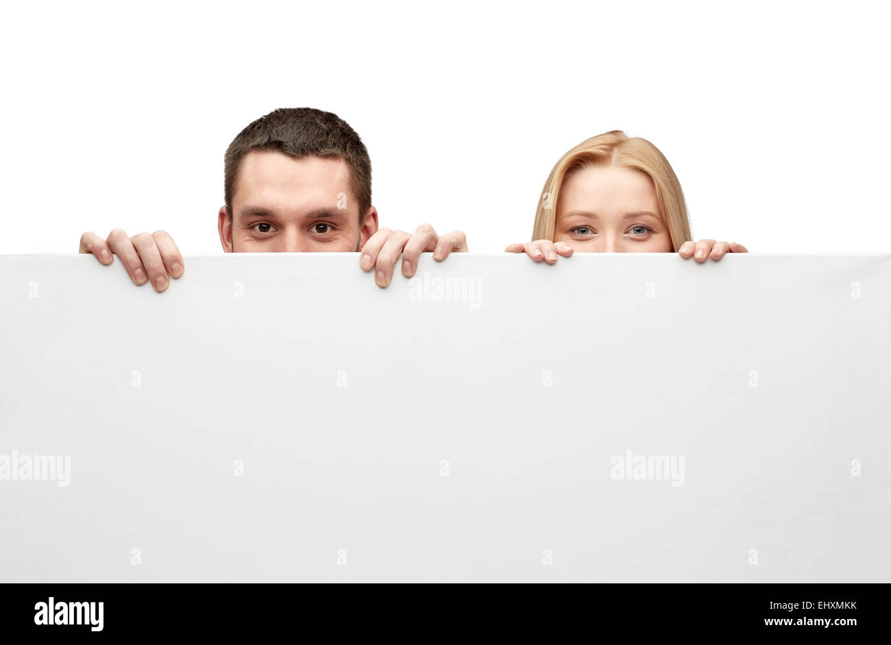 Couple heureux se cacher derrière big white blank board Banque D'Images