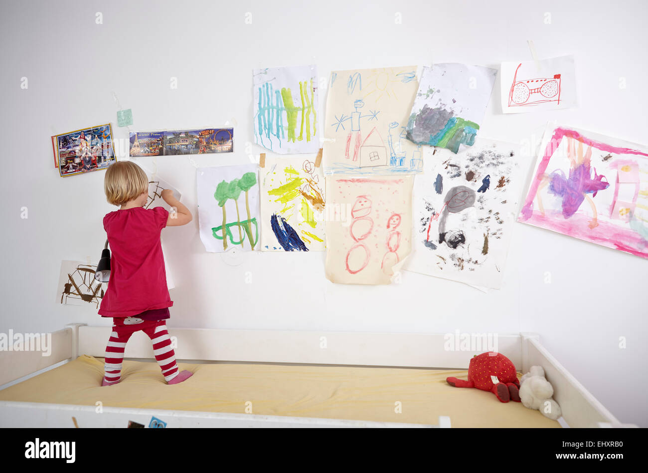 Petite fille peinture sur mur de chambre d'enfants, vue arrière Banque D'Images