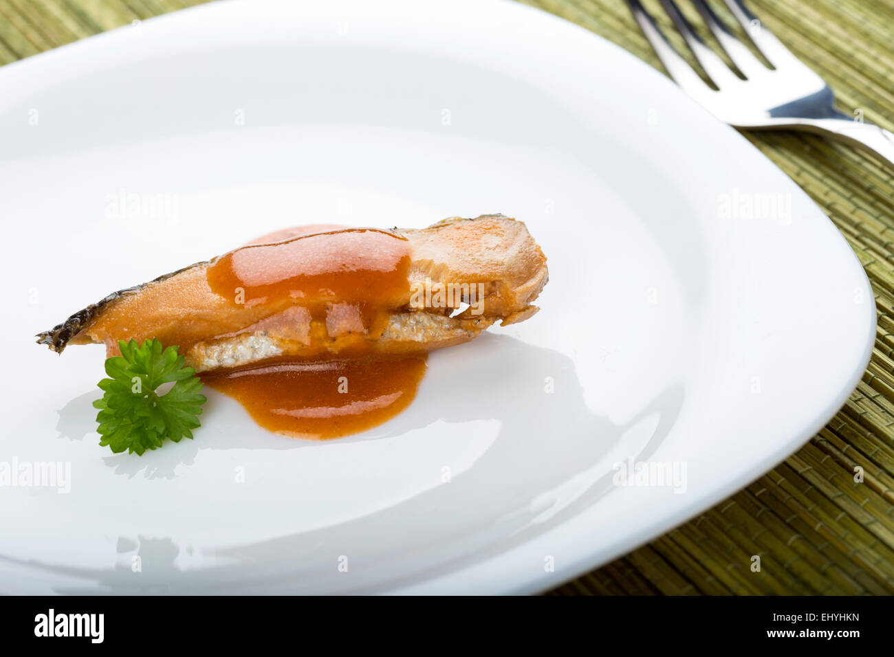 Saumon à la sauce tomate et le persil sur une assiette blanche avec une fourchette Banque D'Images