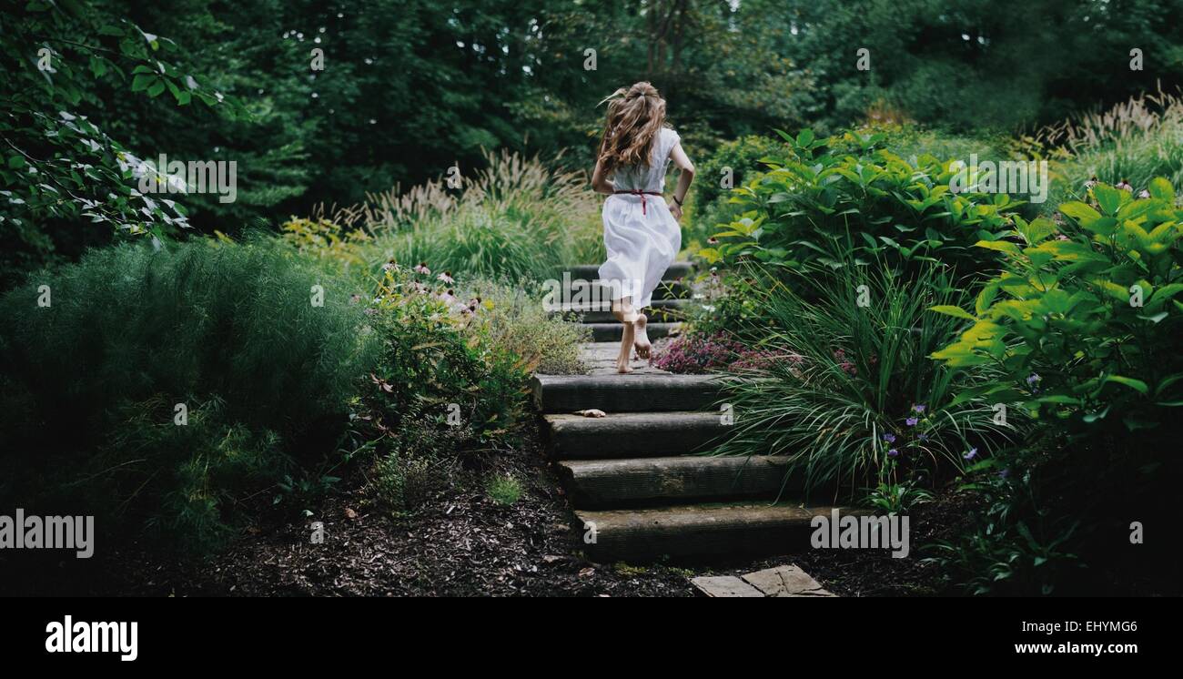 Vue arrière du young woman running up étapes dans un jardin Banque D'Images
