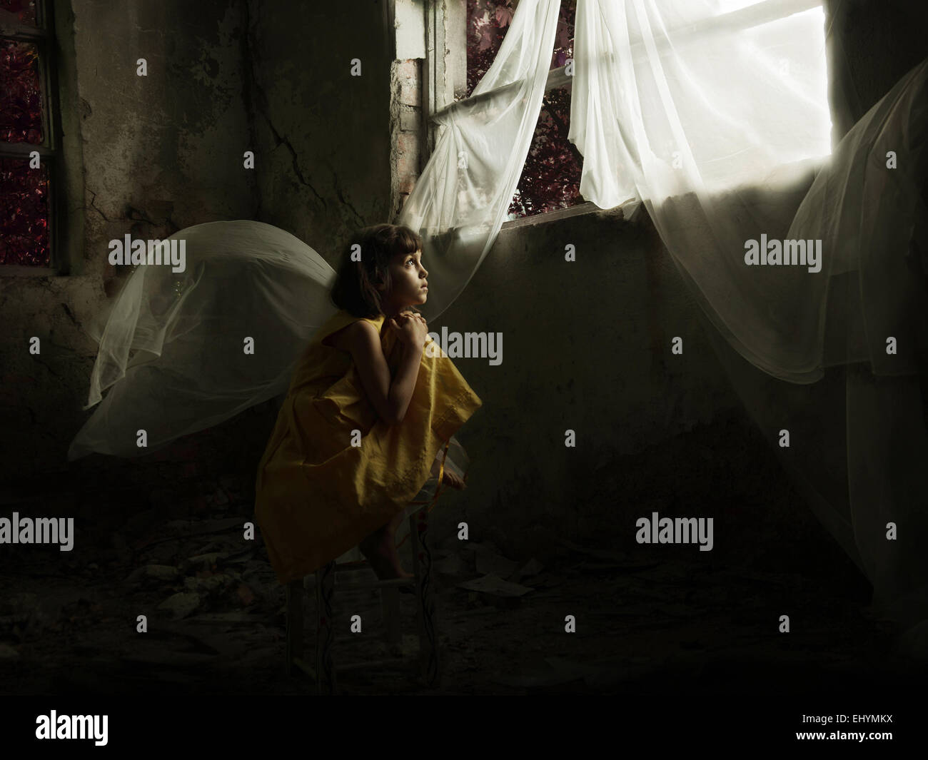 Fille assise sur une chaise, regardant par une fenêtre dans une maison abandonnée Banque D'Images