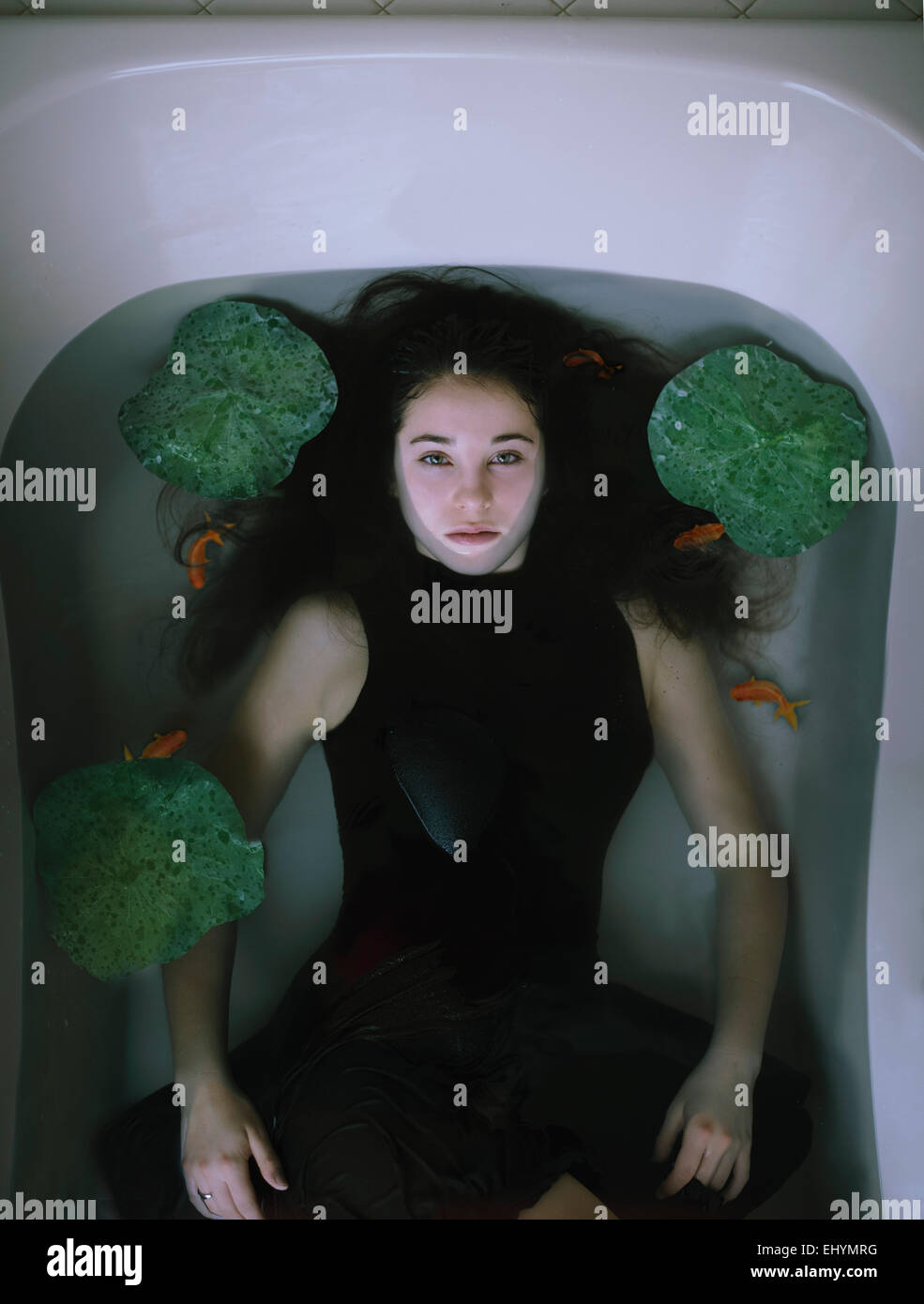 Vue aérienne d'une jeune femme couchée dans une baignoire avec poissons rouges et nénuphars Banque D'Images