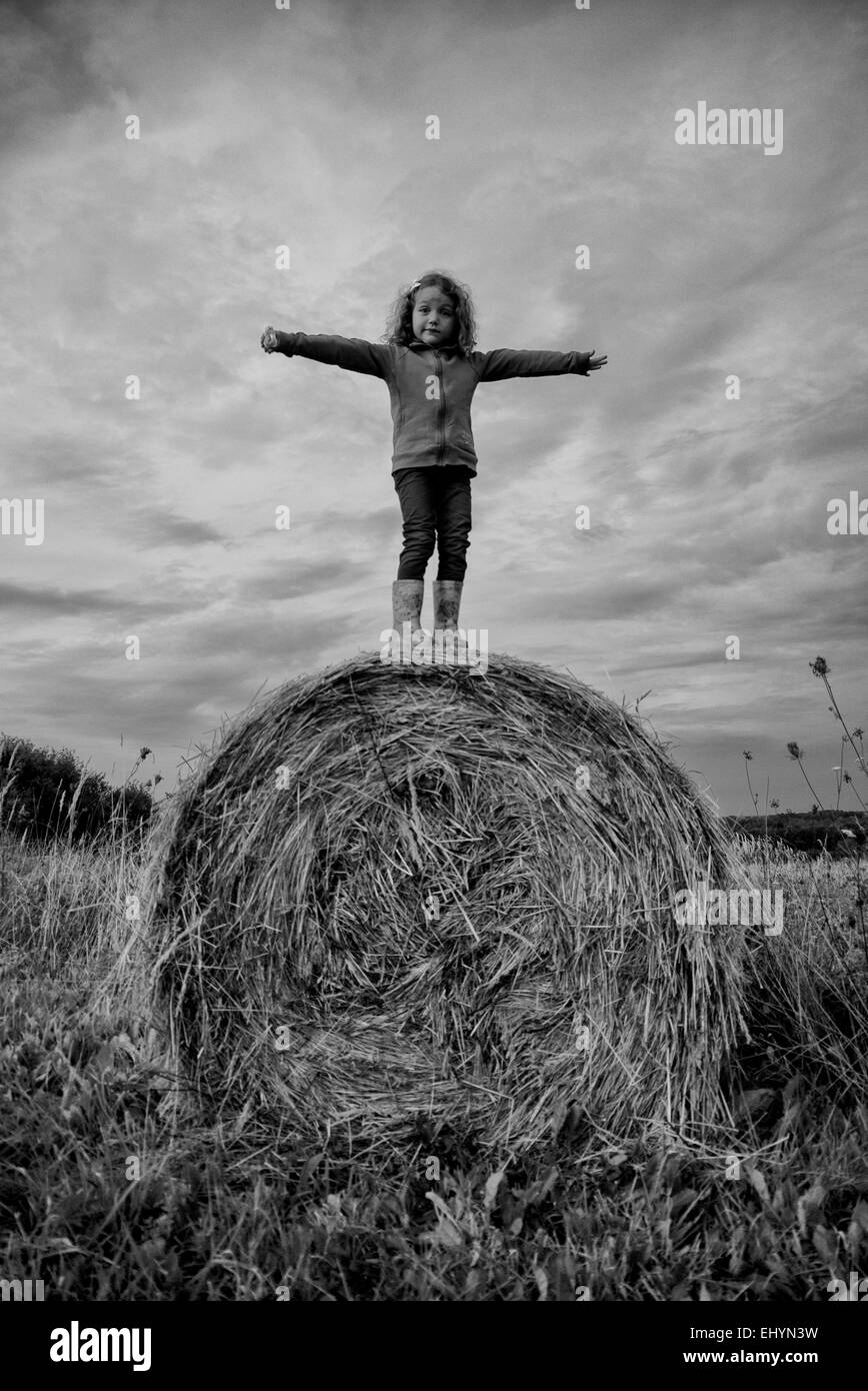 Fille debout sur une balle de foin dans un champ, Pologne Banque D'Images