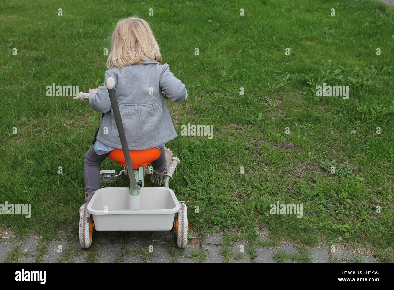 Vue arrière d'une fille sur un tricycle dans le jardin Banque D'Images