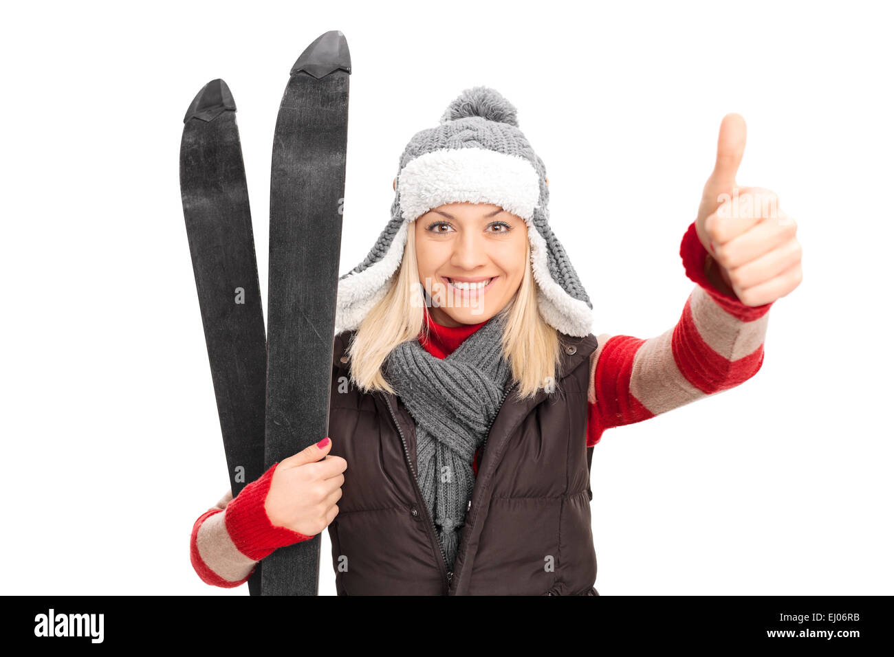 Woman in winter clothes holding skis et giving thumb up isolé sur fond blanc Banque D'Images