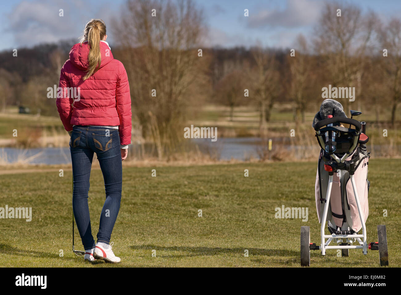 Young woman playing golf retour à son chariot de golf et clubs de l'ensemble de l'allée, vue de derrière Banque D'Images