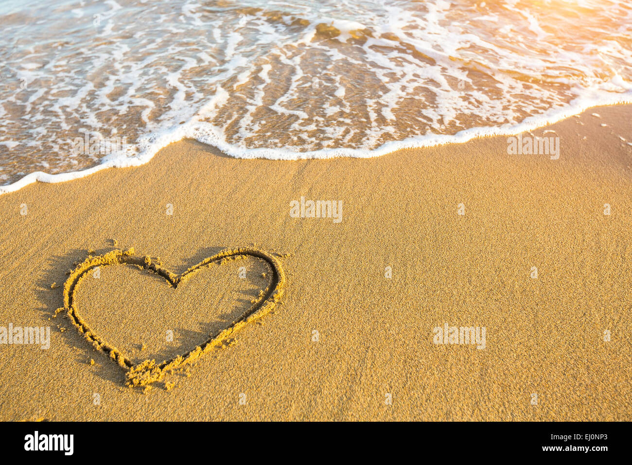 Coeur dessiné à la main sur du sable de plage or doux sur le coucher du soleil. Banque D'Images