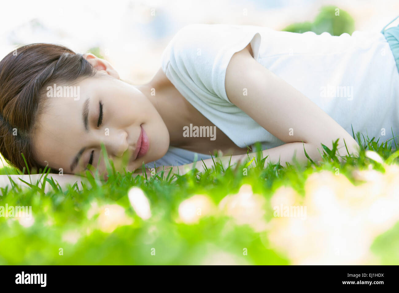 Jeune femme couchée sur le devant sur la pelouse avec les yeux fermés, Banque D'Images