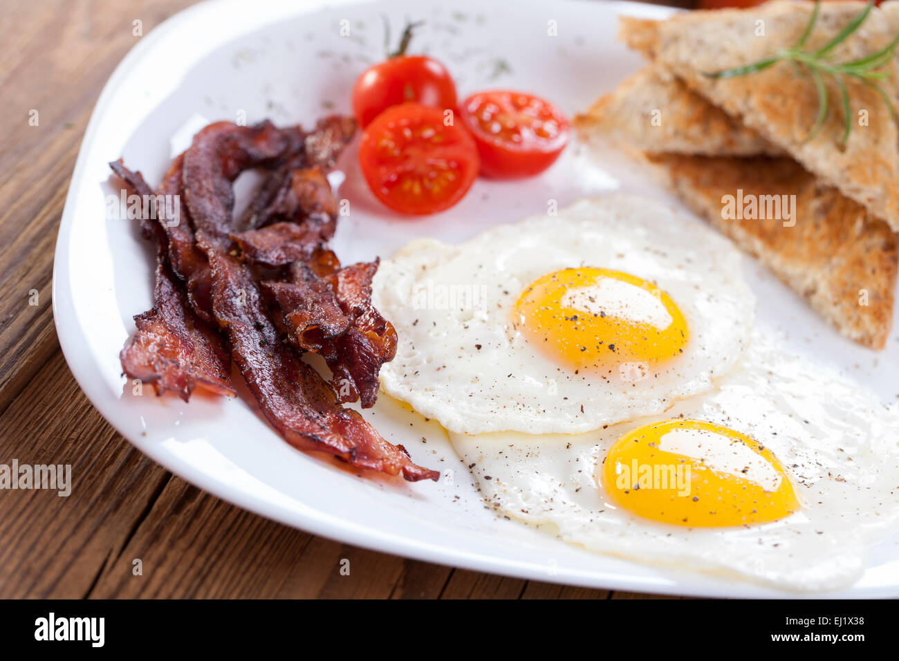 Œuf frit délicieux avec des épices, de bacon, de croûtons et de tomates sur une assiette blanche. Composition sur une table en bois à l'arrière-plan Banque D'Images