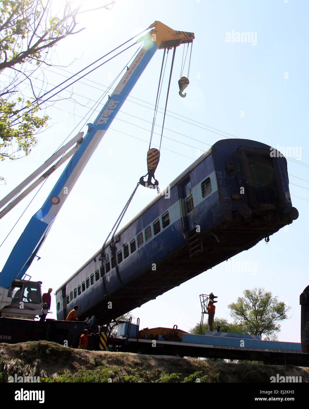 Rae Bareli, Inde. Mar 20, 2015. Un compartiment de train est soulevée par une grue comme la demeure d'un autre tordu est compartiment sur le site d'un accident survenu à Bachhrawan village de la nord de l'état indien de l'Uttar Pradesh, le vendredi 20 mars 2015. La police et les sauveteurs ont utilisé les coupeurs de gaz de déchirer l'épave de trouver des gens qui ont peur d'être pris au piège après trois wagons d'un train de voyageurs a déraillé dans le nord de l'Inde. Au moins 34 personnes ont été tuées et près de 150 autres blessés qui ont résulté de l'accident. Credit : Prabhat Kumar Verma/Pacific Press/Alamy Live News Banque D'Images