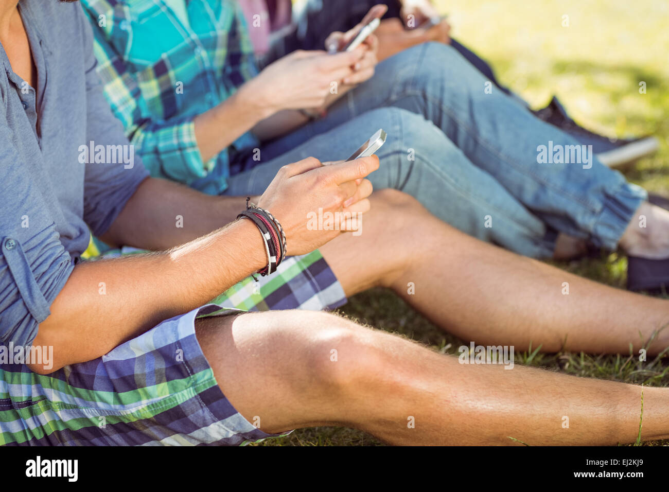 Les gens branchés assis sur l'herbe texting Banque D'Images