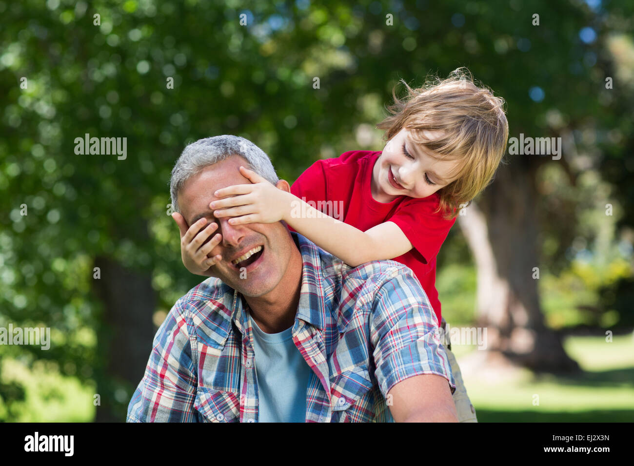Heureux petit garçon cachant ses yeux fatherss avec ses mains Banque D'Images
