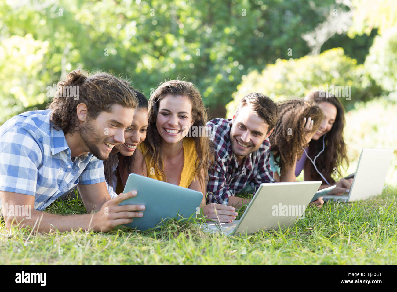 Smiling friends dans le parc à l'aide de Tablet PC et ordinateur portable Banque D'Images