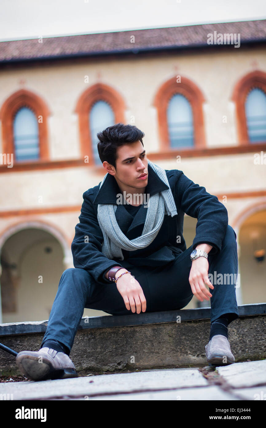 Trendy élégant jeune homme assis en plein air bâtiment historique à la recherche d'un côté. Incliné shot Banque D'Images