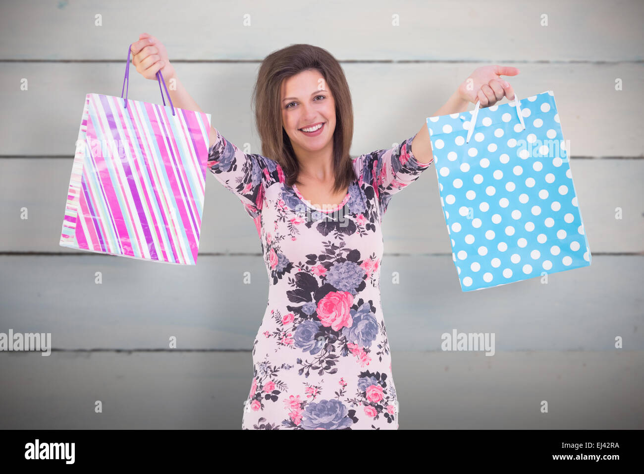 Image composite de jeune femme en robe à fleurs holding up shopping bags Banque D'Images