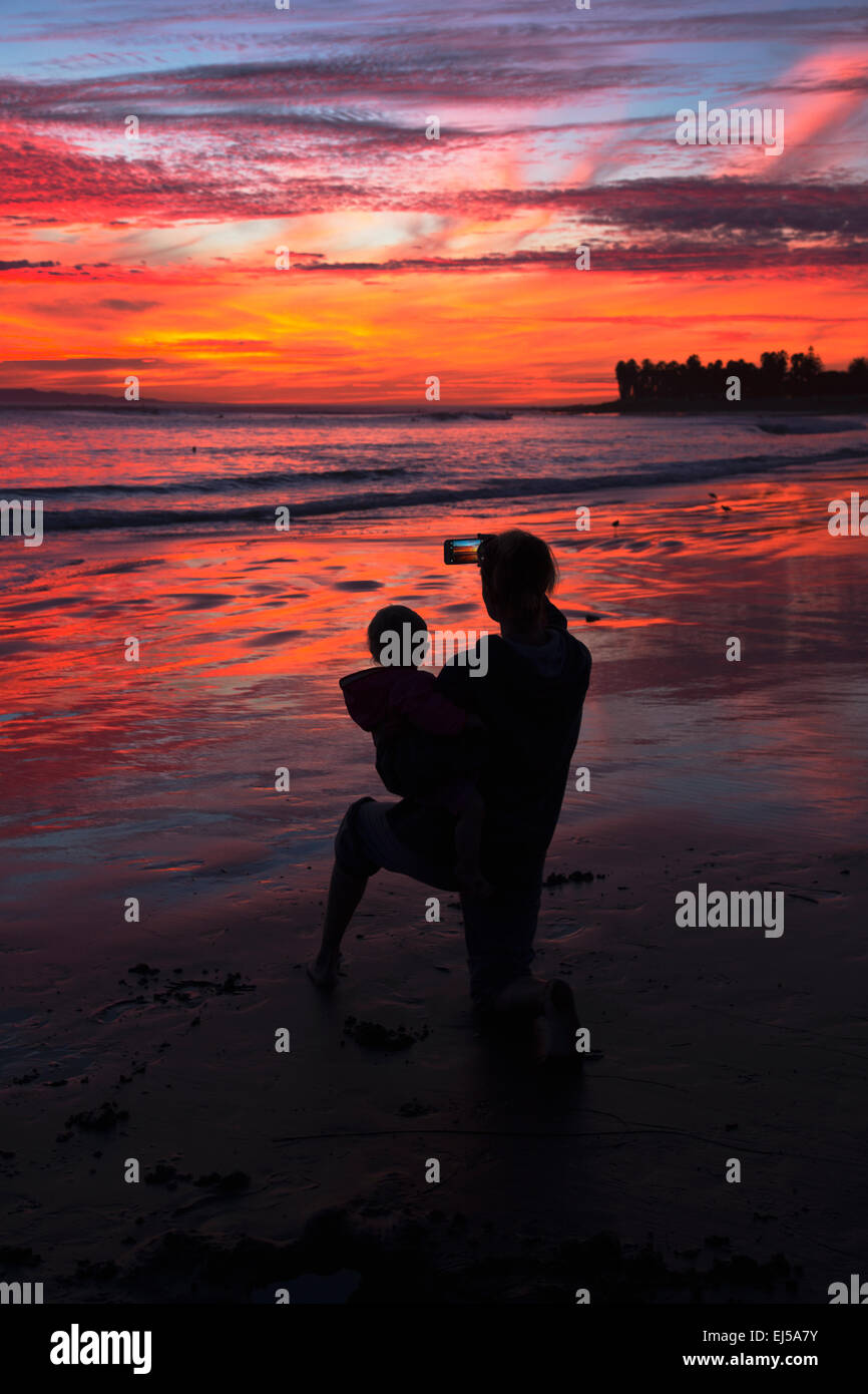 Femme avec enfant prend photo de violet et orange coucher du soleil en regardant vers l'Île Anacapa, Ventura, Californie, USA Banque D'Images