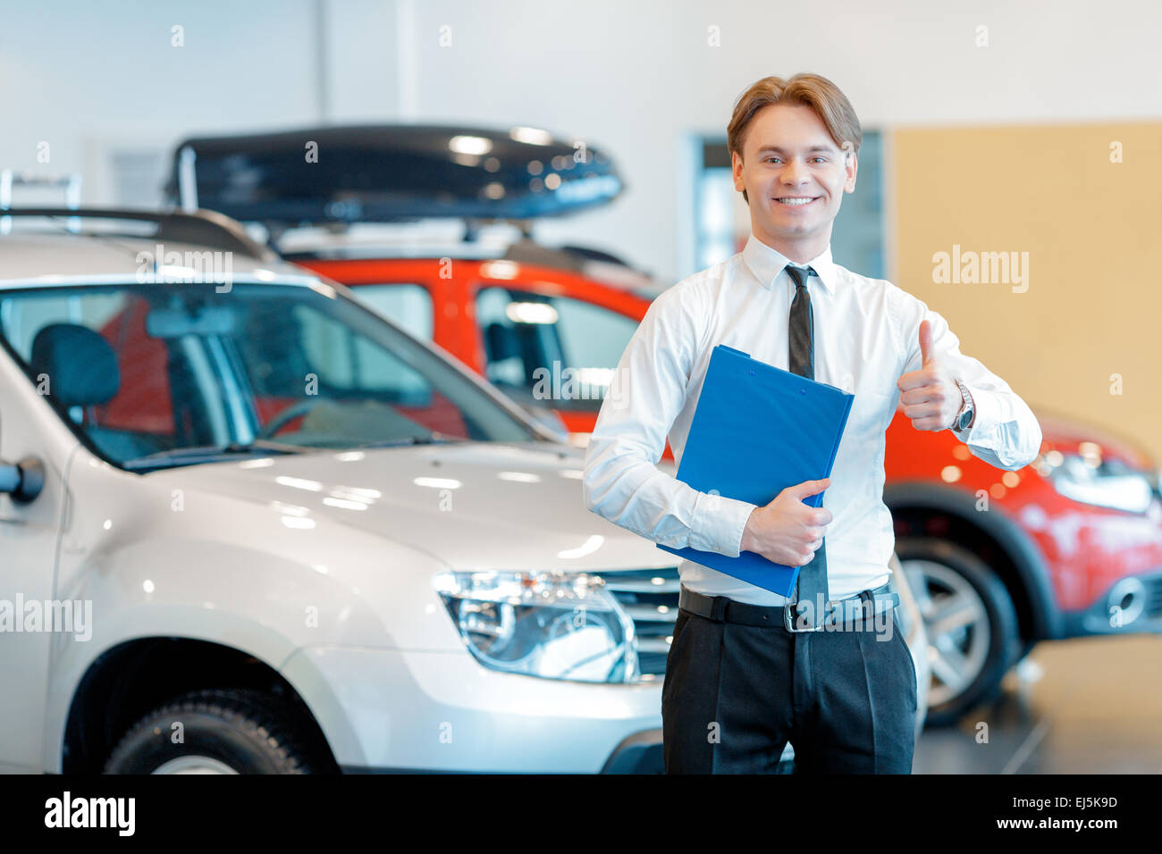 Young smiling salesman with clipboard in car dealership Banque D'Images