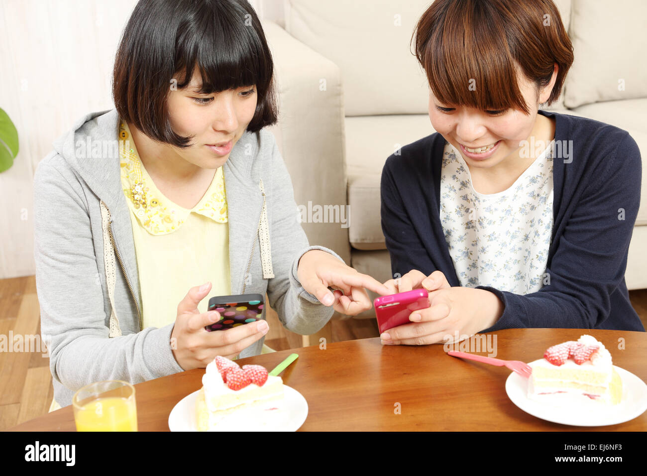 Les jeunes filles japonaises ayant un morceau de gâteau ensemble dans la salle de séjour Banque D'Images