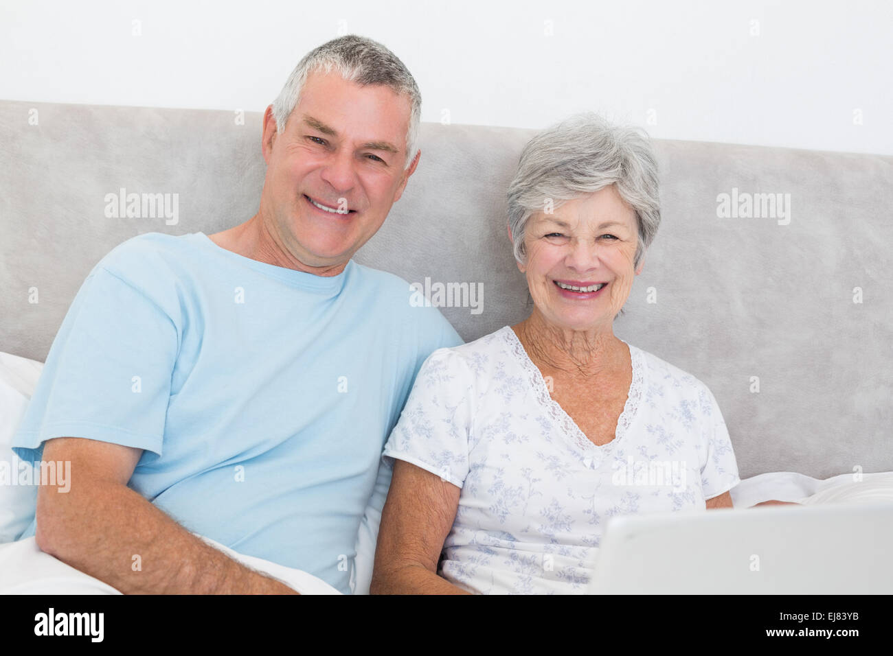 Senior couple with laptop sitting in bed Banque D'Images