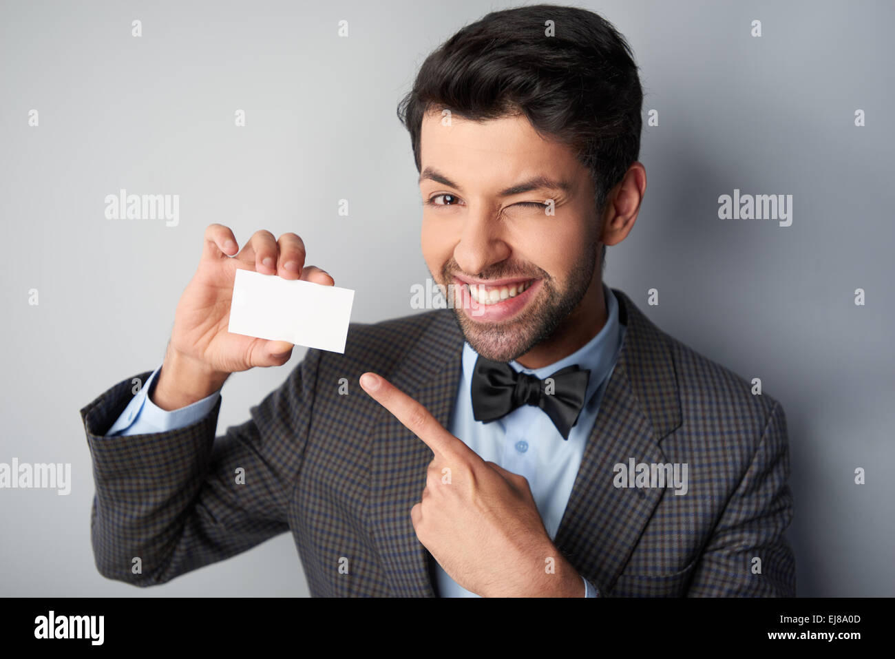Smiling man pointing at carte de visite vierge et clignant de l'oeil Banque D'Images