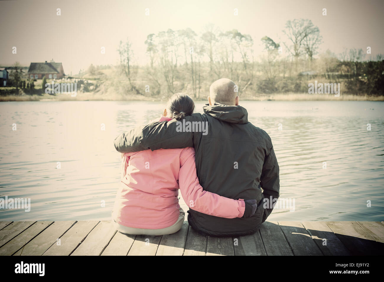 Sépia rétro photo stylisée d'un couple sitting on wooden pier par lac. Banque D'Images