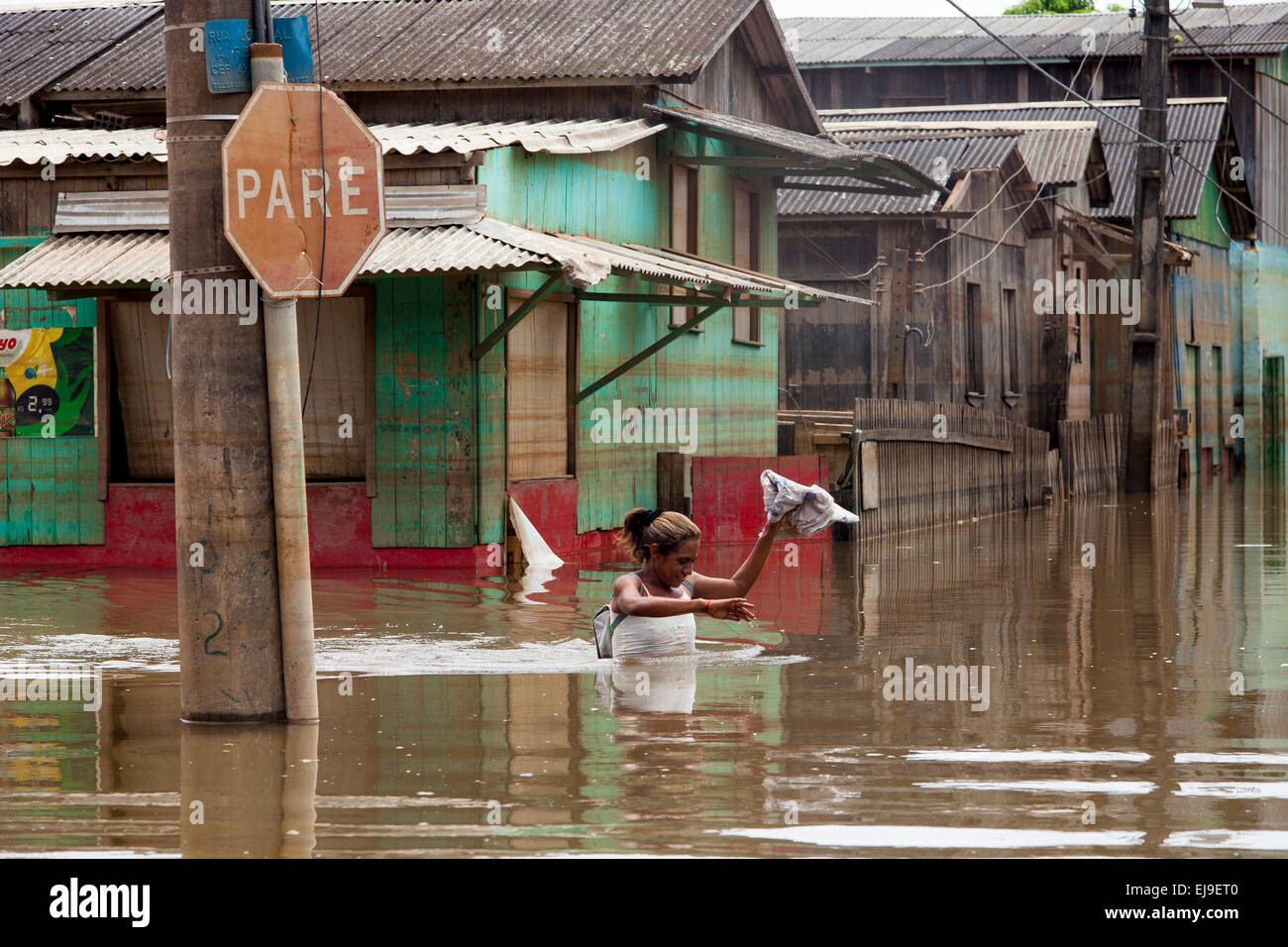 2015 Inondations en Amazonie brésilienne, femme traverse la rue inondée en face d'un panneau d'arrêt ( tape ) à Novo Triangulo, district de la ville de Rio Branco, l'état d'Acre. Les inondations ont touché des milliers de personnes dans l'Etat d'Acre, dans le nord du Brésil, depuis le 23 février 2015, lorsque certaines des rivières de l'état, en particulier l'Acre, la rivière a débordé. De plus fortes précipitations a forcé les niveaux de la rivière plus haut encore, et le 03 mars 2015, le gouvernement fédéral du Brésil a déclaré l'état d'urgence dans l'état d'Acre, où les conditions d'inondations situation a été décrite comme la pire en 132 ans. Banque D'Images